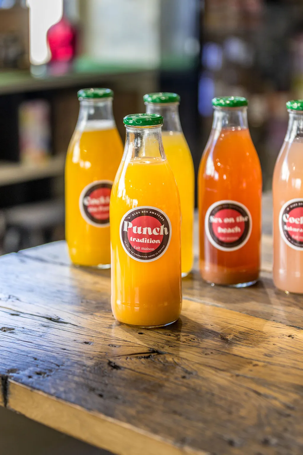 Plusieurs bouteilles de cocktails maison O'Clos alignées sur le comptoir en bois